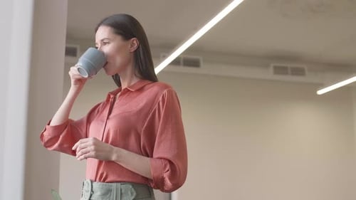 Woman Drinks Coffee Near Window in Bright Workplace