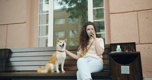 Mujer joven feliz bebiendo té al aire libre en el café y acariciando al lindo cachorro de Shiba Inu