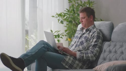 Man Relaxing on Sofa Typing on Laptop