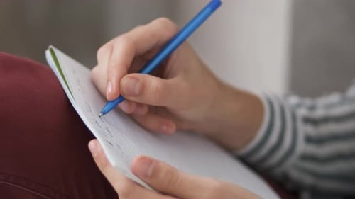 Hands Writing in Notebook With a Blue Pen