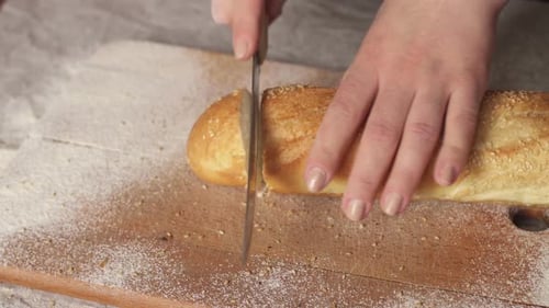 Woman slices fresh bread baguette on cutting board