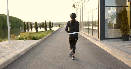 Woman Jogging at Sunset Near Glass Building