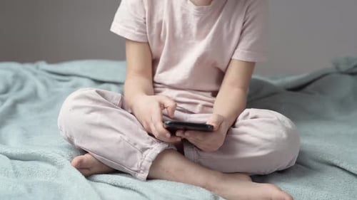 Child Sits on Bed Looking at Phone