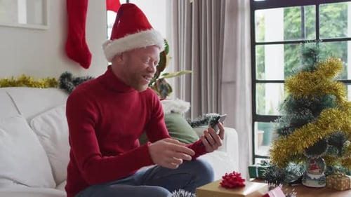 Happy albino african american man wearing santa hat making video call at christmas
