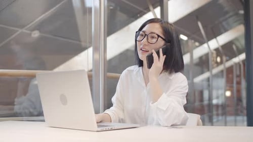 Young Woman Talking on Phone While Using Laptop