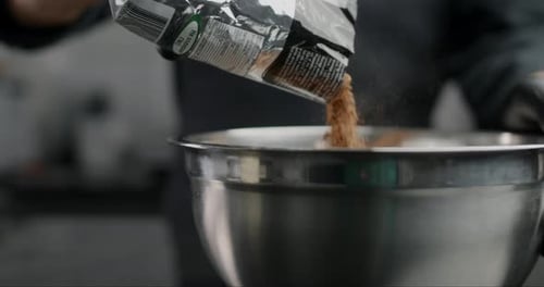 Person pours brown powder into stainless bowl