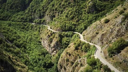 Flying Drone Over Mountains with Winding Mountain Road and Forest