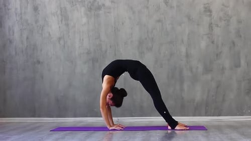 Frau in schwarzer Sportkleidung macht Yoga auf einem lila Teppich im Studio mit natürlicher Weihe