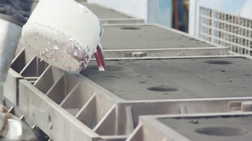 Workers in a foundry pouring liquid Aluminum to a sand cast