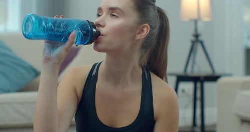 Woman Drinks Water from Blue Bottle at Home