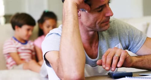 Man Using Calculator With Children in Background