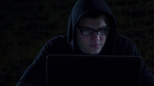 Hooded Man Using Laptop in Dark Room