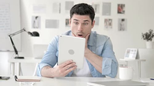 Man Looks at Tablet in Bright Office, Surprised