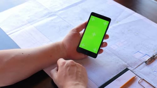 Construction engineer using a smartphone with a green screen looking for information on the internet