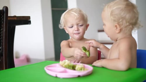 Two Toddlers Eating Broccoli at a Table