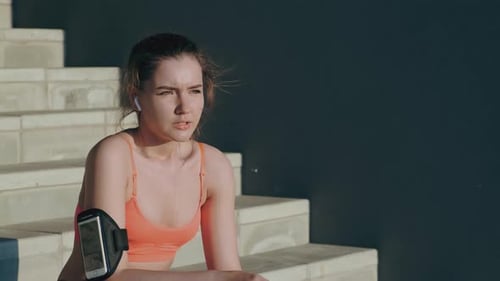 Chica con teléfono en el brazo se sienta en los escalones después de correr a cámara lenta