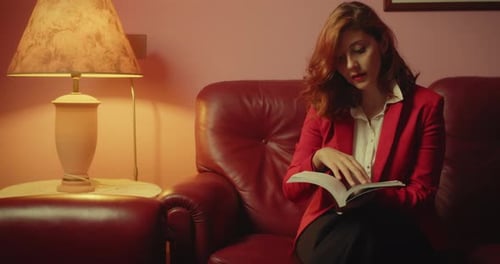 Stylish Young Woman Reads a Book on a Couch