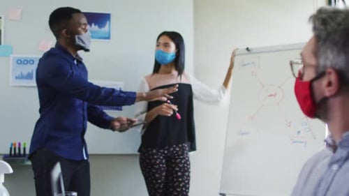 Diverse male and female office colleagues wearing face masks giving presentation at modern office