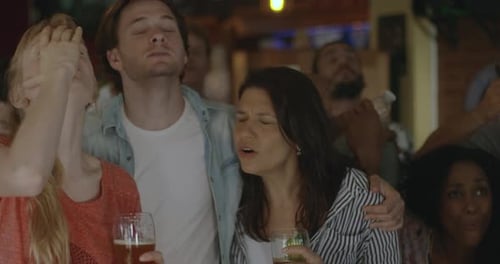 Sports enthusiasts reacting to defeat while watching televised match in bar, slow motion