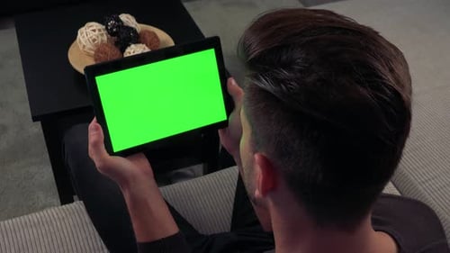 A Man Watches a Tablet with a Green Screen, Horizontally, in Living Room