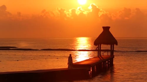 Woman walks along dock during sunset at tropical resort