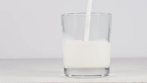 Pouring fresh milk in glass over white background