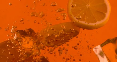 Lemon Slices and Ice Cubes Falling into Orange Juice