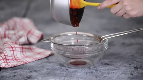 Hands Straining Red Juice Into Glass Bowl