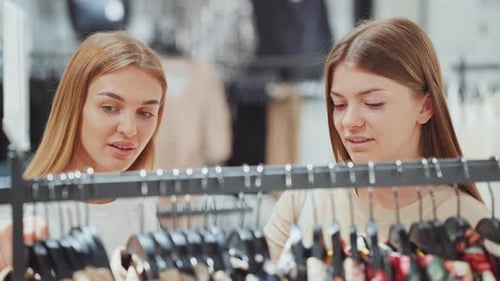 Women Friends Looking at Clothes on Hangers at Store