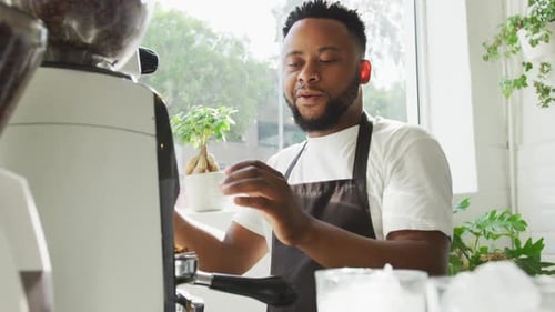 Happy african american male barista making coffee using coffe machine at cafe