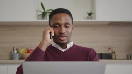 Close Up of a Young Adult Businessman Having a Call on His Phone in Front of His Laptop