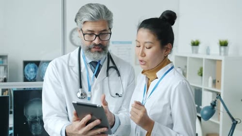 Male and Female Doctors Looking at Tablet Screen Talking and Smiling Indoors in Modern Clinic