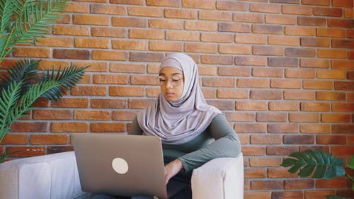 Woman Uses Laptop In Front of Brick Wall