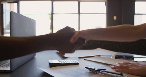 Close-up of young mixed-race business team shaking hands and sitting at desk of modern office 4k