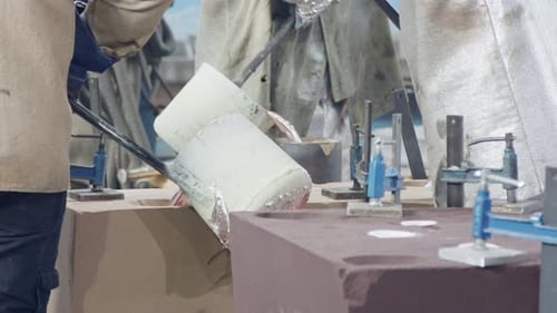 Workers in a foundry pouring liquid Aluminum to a sand cast