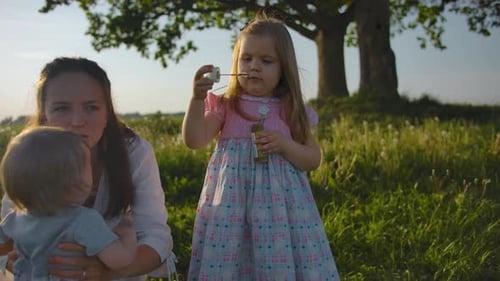 Mother and Children Blowing Bubbles in Green Field