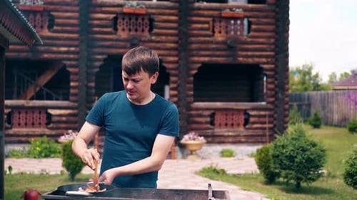 Young Man Makes Pilaf in a Cauldron on a Grill on an Open Fire