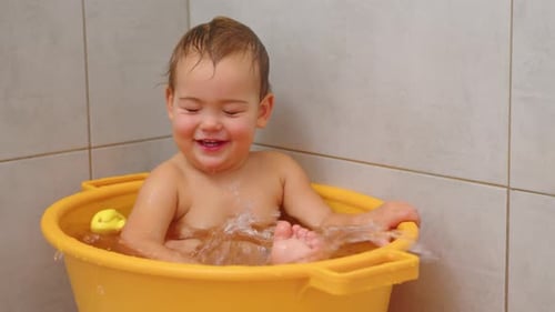 Joyful Infant Plays in a Yellow Bath Tub