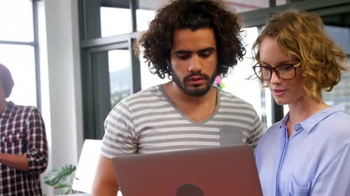 Man and Woman Reviewing Laptop in Modern Office