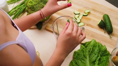 Woman Putting Cut Cucumber Into Blender Closeup Cooking Green Detox Smoothie in the Kitchen