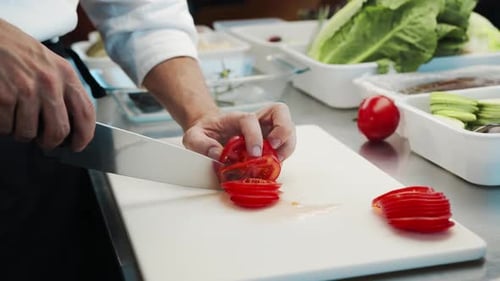 Professional restaurant kitchen, close-up: Chef cuts tomatoes with a knife