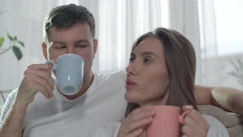 Couple Relaxing Together, Drinking from Mugs Indoors