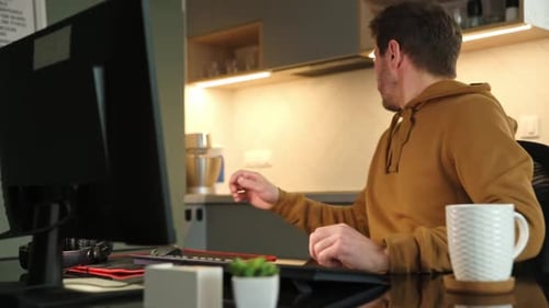 Man Working at Computer, Eating Toast at Desk