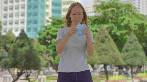 A Young Woman on the Street Puts on an Already Used Face Mask on Her Face. Do Not Reuse Single-use