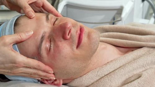 Hübscher Mann lächelt in die Kamera und erhält Gesichtsmassage im Spa-Center