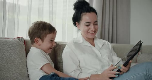 Smiling Mother and Child Interact with Tablet on Couch