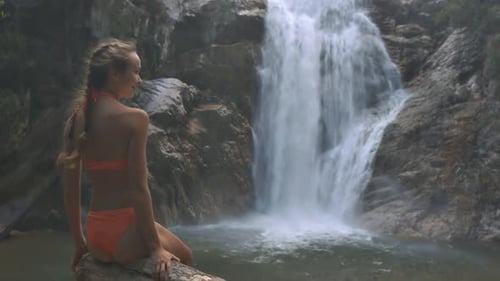 Woman Sits near Tropical Waterfall in Nature