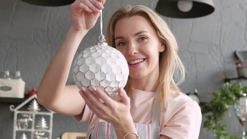Blonde Holds Christmas Decoration and Smiles. close-up.Girl Shows a Product and Holds a Toy Ball