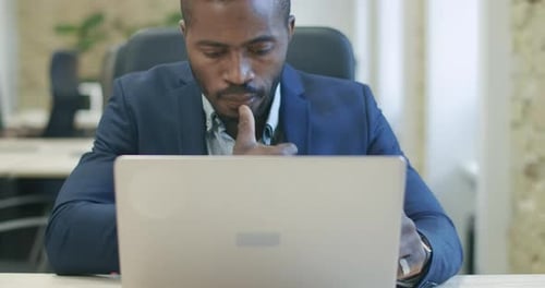 Apuesto empresario afroamericano concentrado que trabaja en línea con una computadora portátil. Retrato de