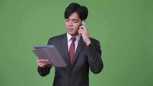 Young Adult Businessman Talks on the Phone with Tablet